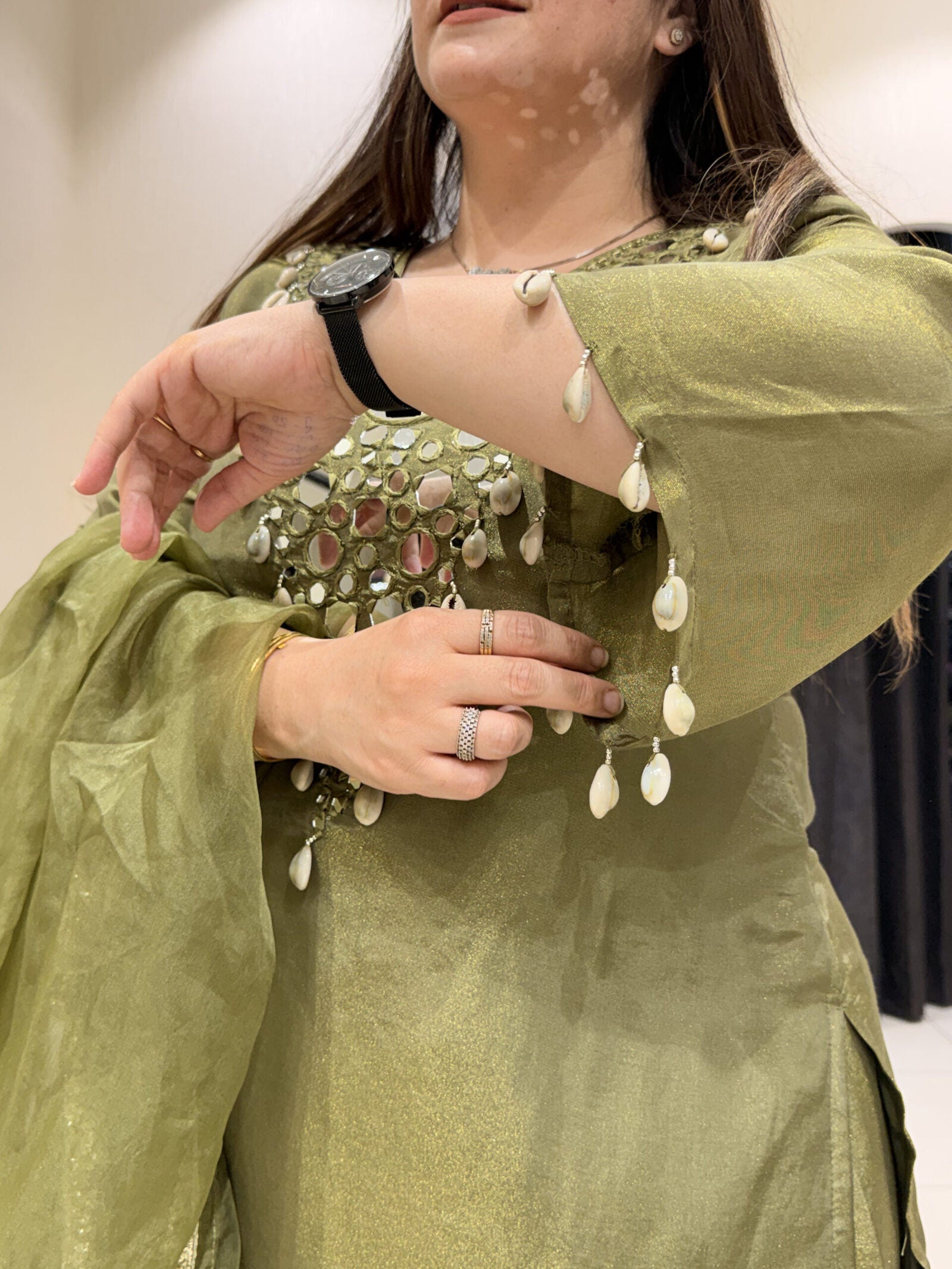 Woman in an olive green co-ord set with shell embellishments and mirror work