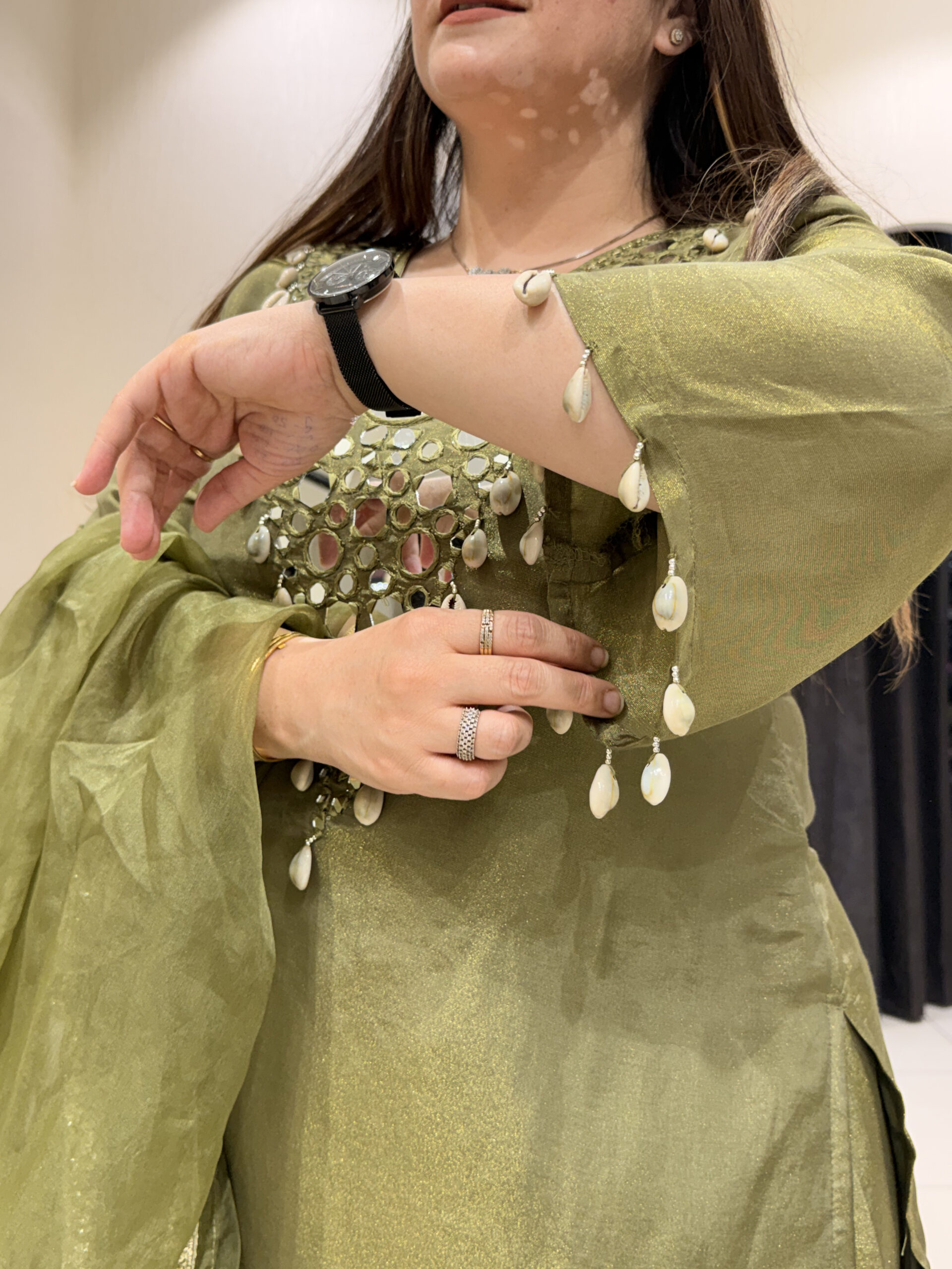 Woman in an olive green co-ord set with shell embellishments and mirror work